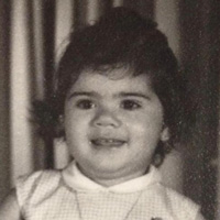 Foto em preto e branco de Lis Leão quando criança. Ela sorri para a foto, tem cabelos curtos e usa uma roupa clara.