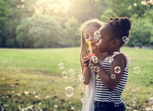duas meninas brincam de fazer bolhas de sabão ao ar livre.