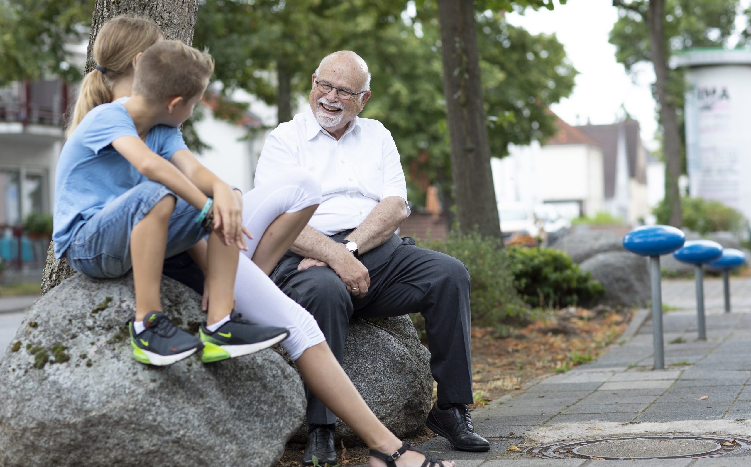 Bernhard Meyer, autor do livro Cidades para Brincar e Sentar, conversando com crianças, sentados sobre pedras em uma calçada na Alemanha.