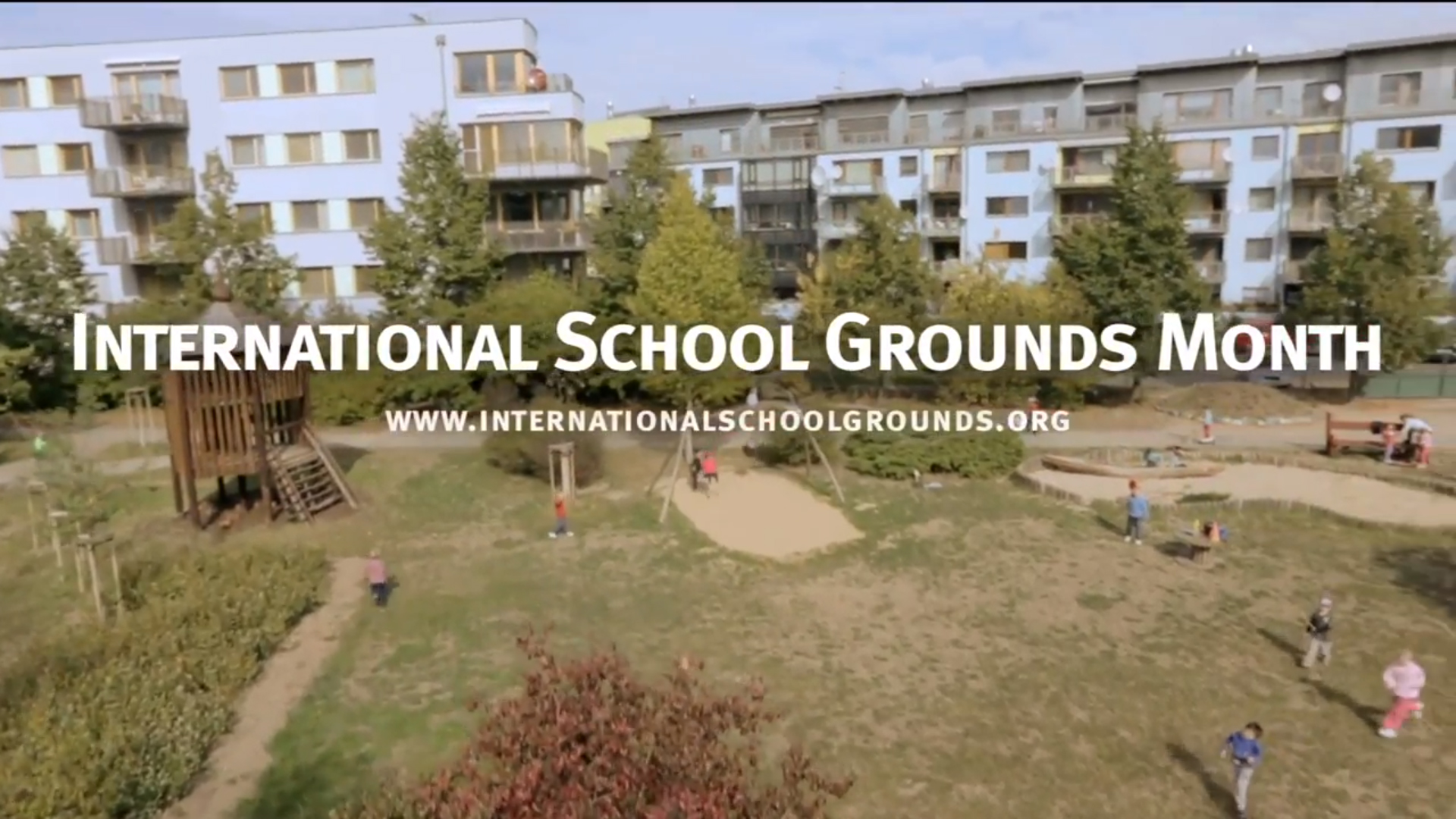Vista aérea de um pátio escolar gramado e arborizado com crianças brincando, ao fundo alguns prédios. Sobre a imagem está escrito em branco 
