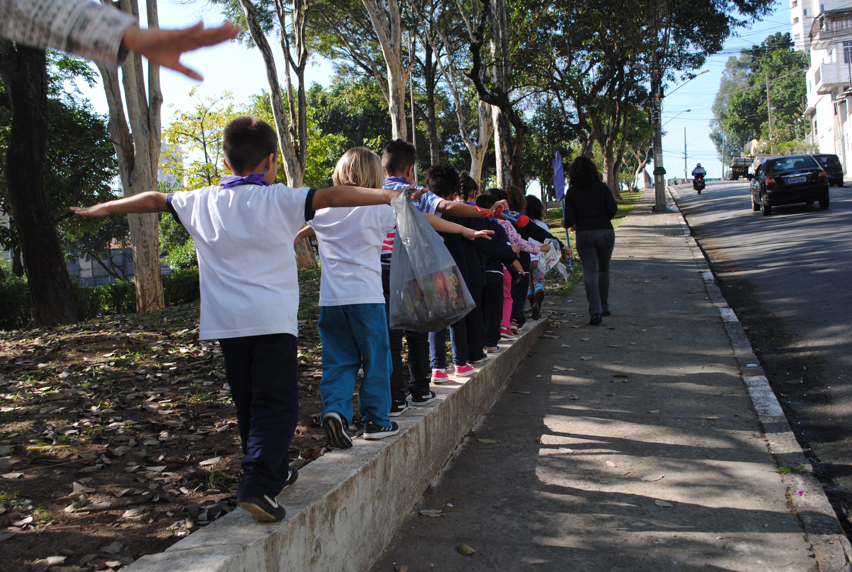 Grupo de crianças caminha sobre mureta na beira da calçada.