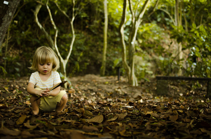 Criança está agachada em meio a folhas brincando com um galho.