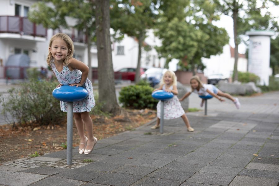 Três meninas brincam nos acompanhantes de caminho instalados na calçada.