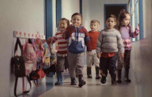 Crianças pequenas caminham empolgadas por um corredor na escola.