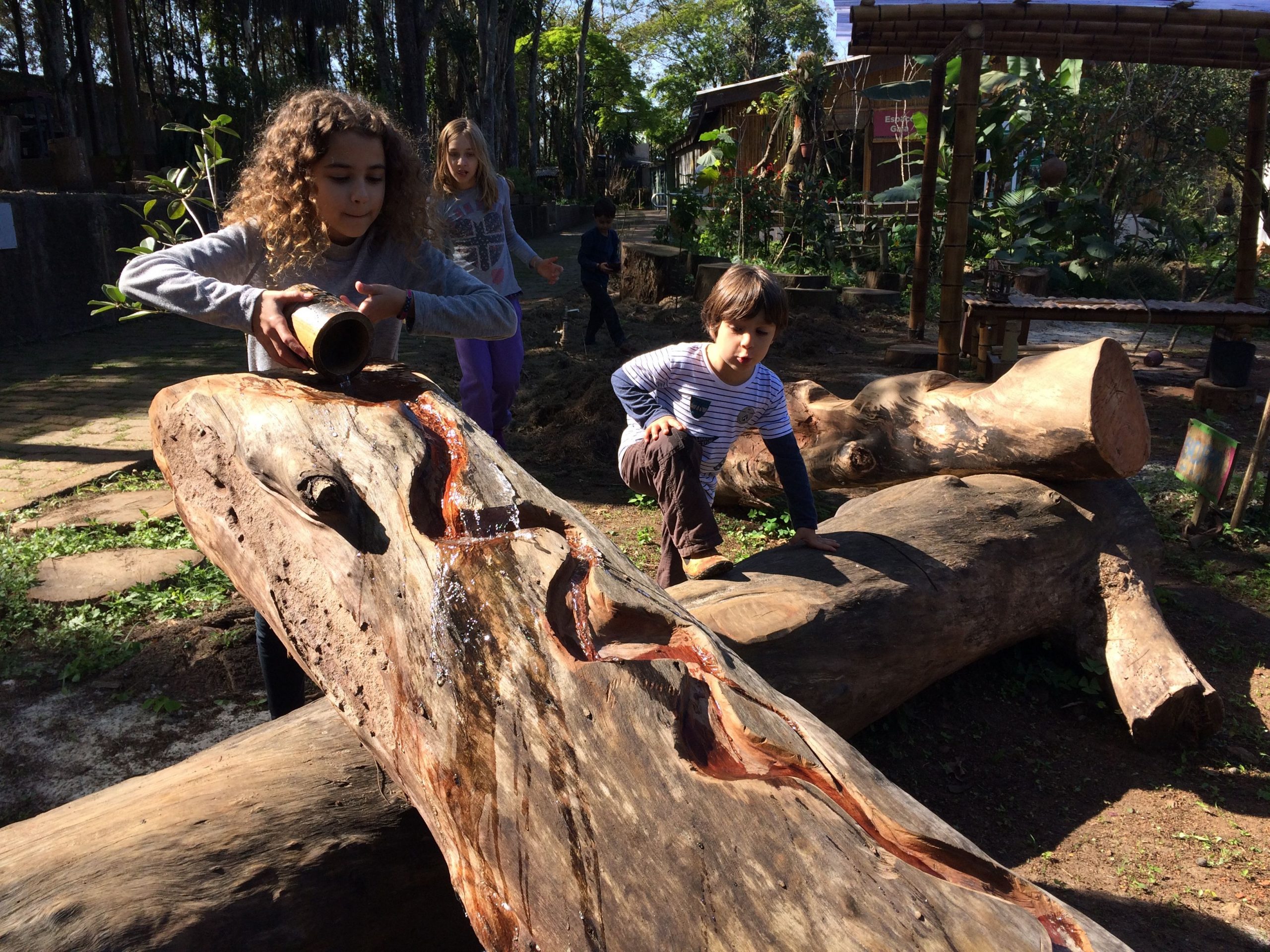 Crianças brincam em espaço composto com troncos de diferentes tamanhos e formas.