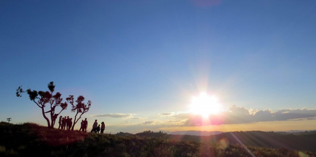 Grupo de pessoas obeservando o por do sol no alto de uma montanha.