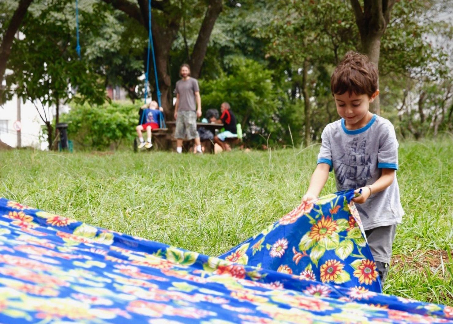 Criança estendendo uma toalha de piquenique na grama.