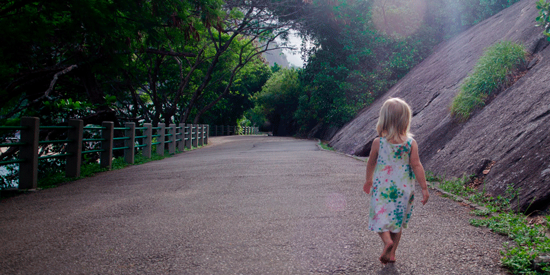 Criança caminhando ao ar livre, cercada por natureza.