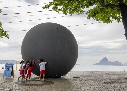 grupo de crianças empurrando uma bola cinza inflável gigante.