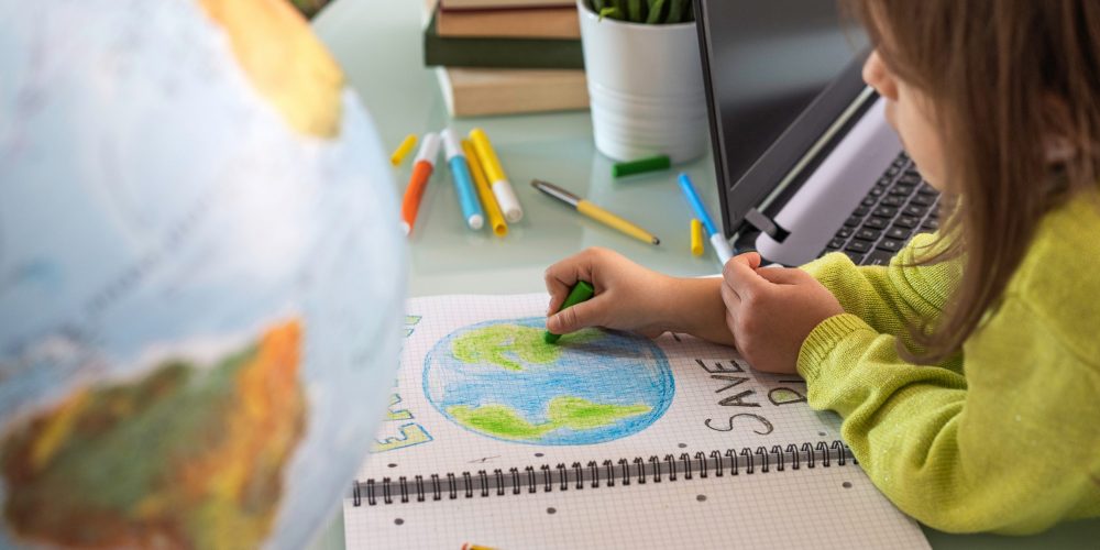 Criança desenhando com giz colorido o planeta Terra em um caderno.