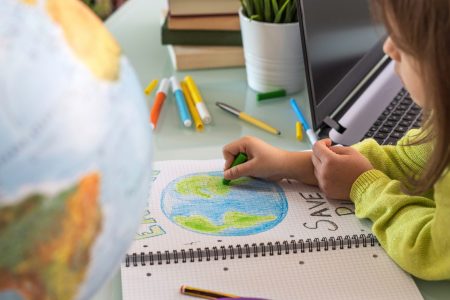 Criança desenhando com giz colorido o planeta Terra em um caderno.