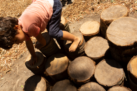 Criança brincando sobre troncos de madeira de diferentes tamanhos e agrupados.