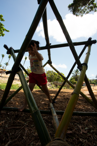 Criança saltando entre estrutura de um brinquedo feito de bambu, semelhante a uma estrela.
