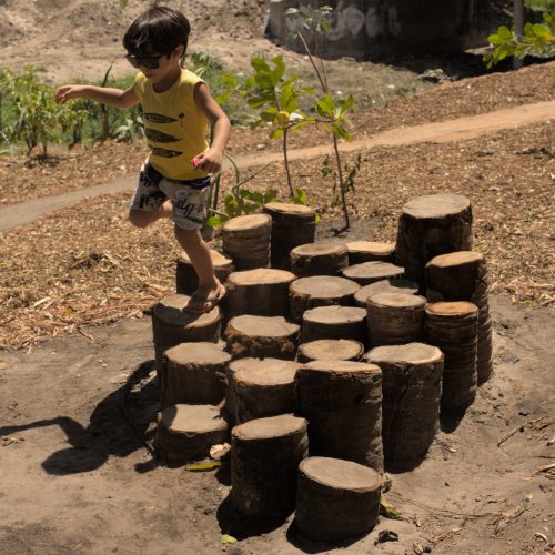 Criança saltando de um brinquedo construído de tocos de madeira de diferentes alturas.