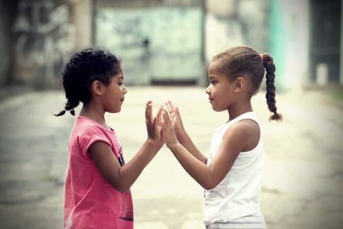 duas meninas brincam batendo as mãos, uma em frente à outra