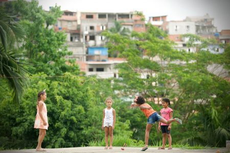 Quatro meninas brincam em Carapicuíba, na periferia de São Paulo, tendo as construções do bairro ao fundo