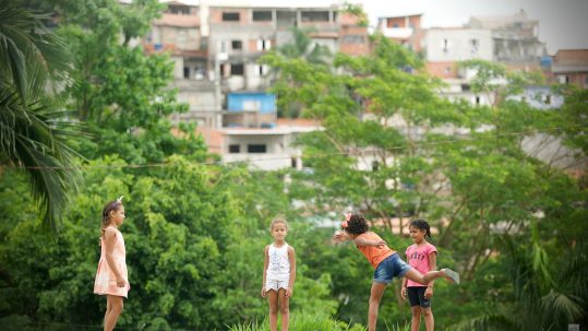 Quatro meninas brincam em Carapicuíba, na periferia de São Paulo, tendo as construções do bairro ao fundo